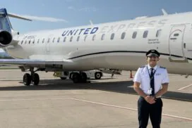 Smiling uniformed pilot standing on tarmac in front of a United Express regional jet with engines and fuselage visible