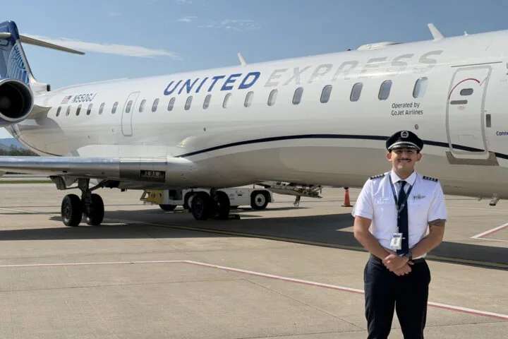 Smiling uniformed pilot standing on tarmac in front of a United Express regional jet with engines and fuselage visible