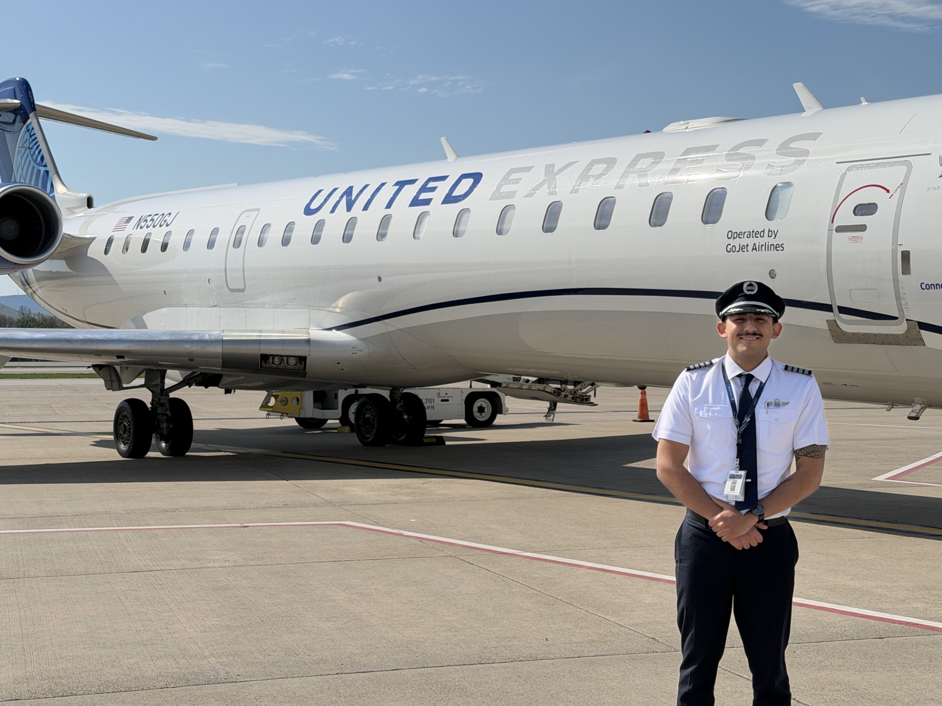 Smiling uniformed pilot standing on tarmac in front of a United Express regional jet with engines and fuselage visible