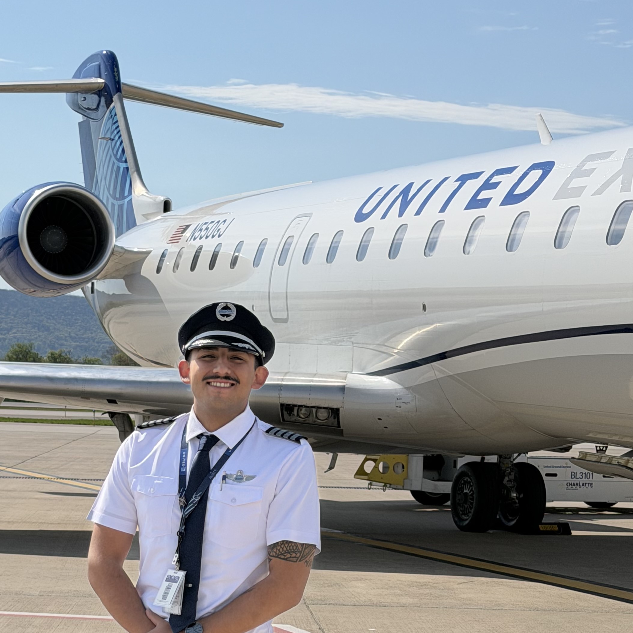 Smiling pilot in uniform standing in front of a United Express regional jet with engine and tail visible